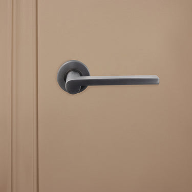 Lavuzo Caserta deurklink Gun Metal PVD gecoat op rond rozet gemonteerd op beige deur, vooraanzicht