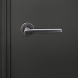 Caserta PVD gecoate binnendeurkruk Gun Metal met rond rozet op donkere deur, vooraanzicht