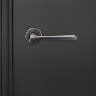 Caserta PVD gecoate binnendeurkruk Gun Metal met rond rozet op donkere deur, vooraanzicht