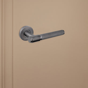 Gekartelde Gun Metal Cosenza binnendeurklink van Lavuzo op beige achtergrond, linkeraanzicht