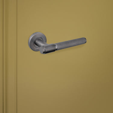 Gun Metal deurgreep Cosenza met kartelmotief op ronde rozet van Lavuzo op groene deur, linkeraanzicht