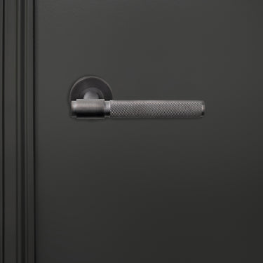 Cosenza PVD gecoate binnendeurkruk Gun Metal met Knurled motief op donkere deur, vooraanzicht