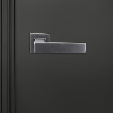 Imperio PVD gecoate binnendeurkruk Gun Metal met vierkant rozet op donkere deur, vooraanzicht