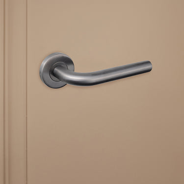 Elegant gebogen Gun Metal Oristano binnendeurklink van Lavuzo op beige achtergrond, linkeraanzicht