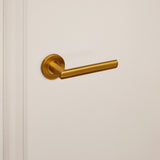 Gouden Ragusa deurkruk van Lavuzo met rond rozet op crèmekleurige deur, linkeraanzicht